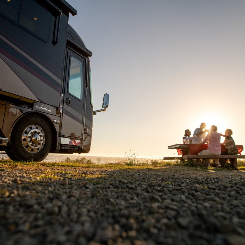 two couples cheersing drinks at sunset next to an Entegra Anthem motorhome 