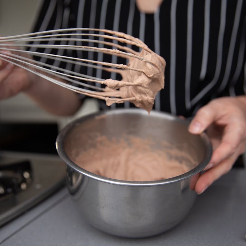 A woman holding a whisk up to show the chocolate whipped cream she's just prepared.