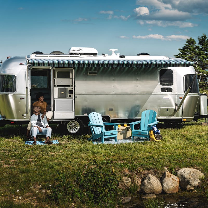 A couple sits at the steps of an Airstream travel trailer