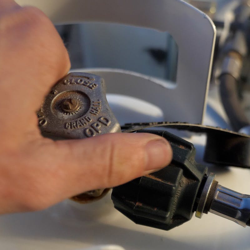 A hand on the knob of a propane tank, showing it in the closed position.