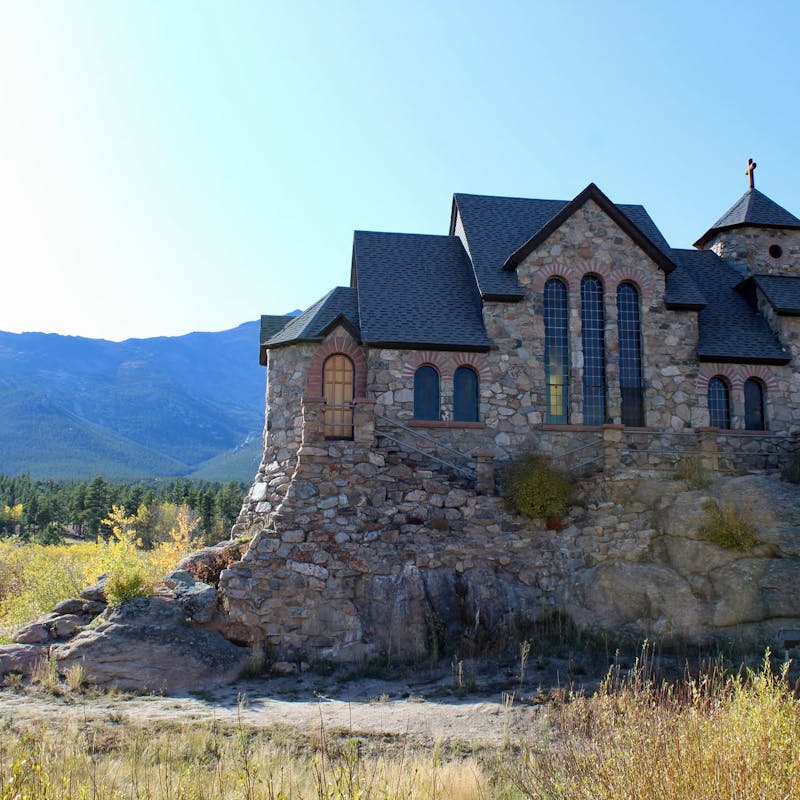 Stone church in the middle of a grassy field surrounded by mountains