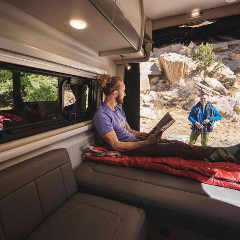 A man sits on the bed of a Class B RV