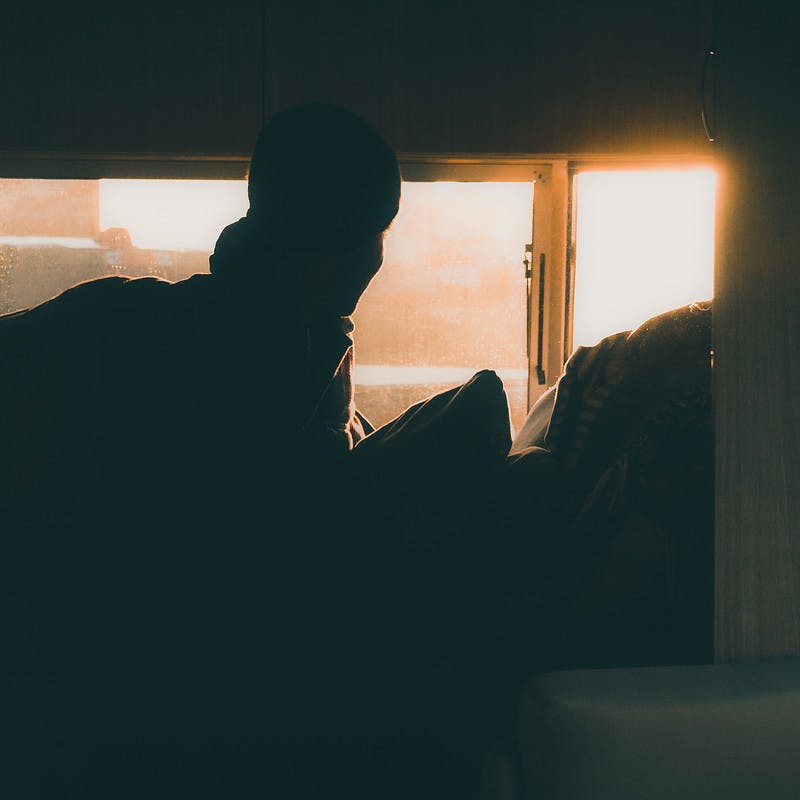 Early morning sun shines in an RV window onto a person still in bed.