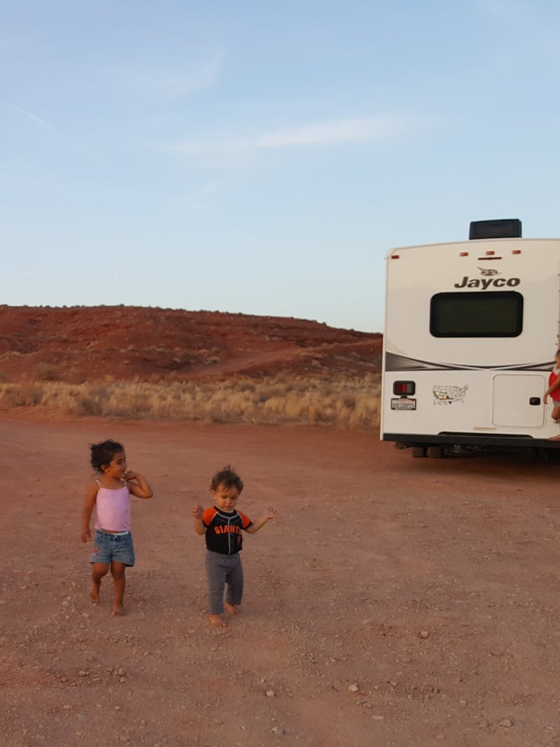 Sandra Peña's kids run around outside on a dirt road in front of her Jayco Class C RV. 