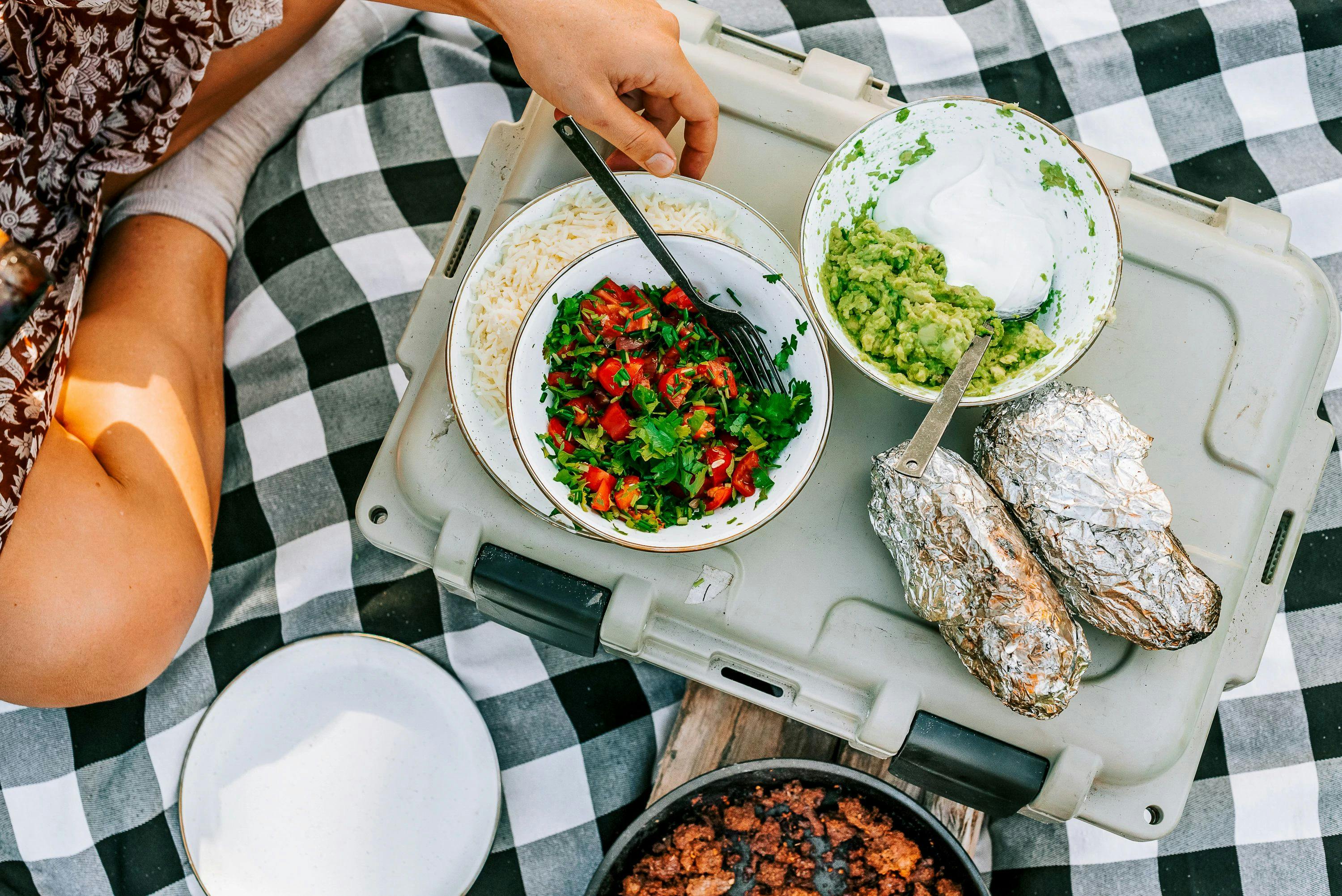 Toppings of fresh salsa and quacamole in a bowls set next to potatoes wrapped in foil