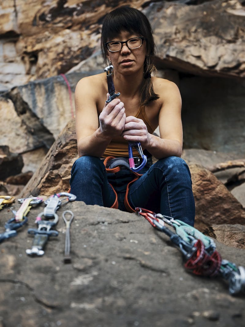 Kathy Karlo holding up climbing gear while sitting on a rock
