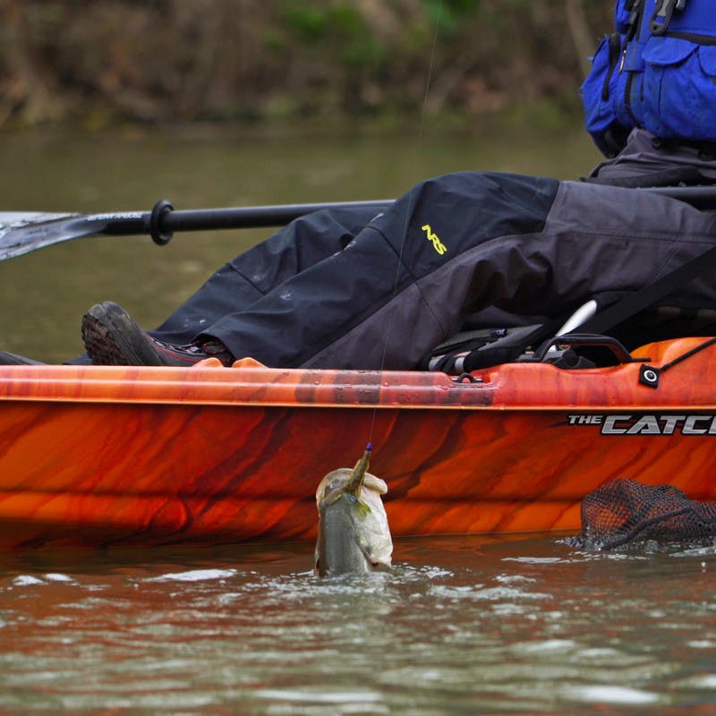 Pulling a fish out of the water from a red kayak.