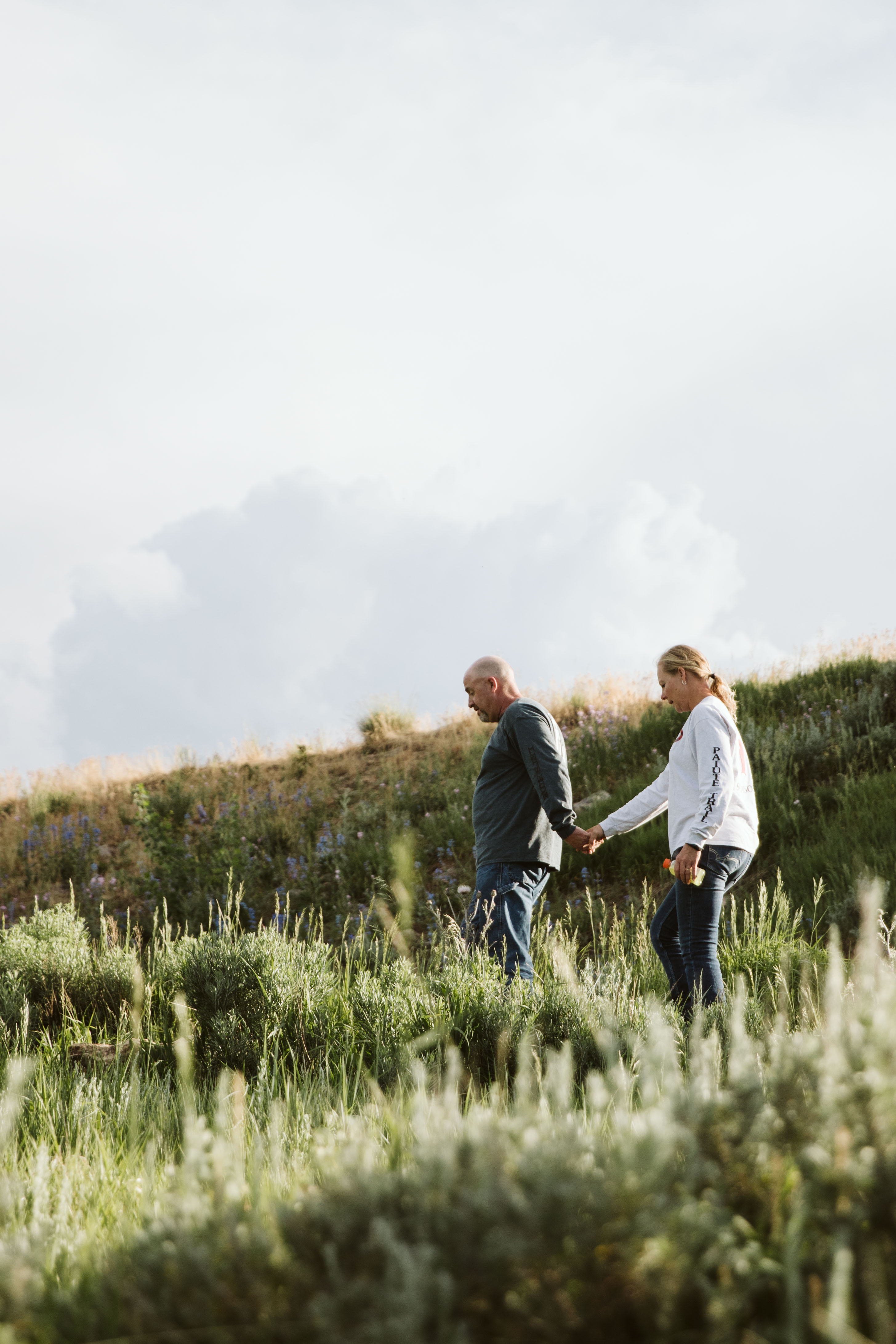 A couple holds hands walking down a scenic trail. 