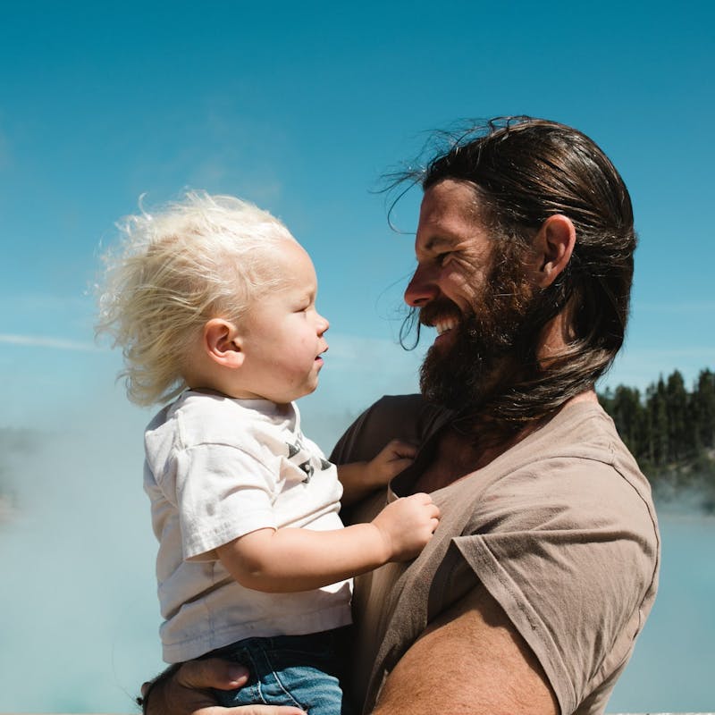 Father holds son and looks at each other in front of steaming hot springs