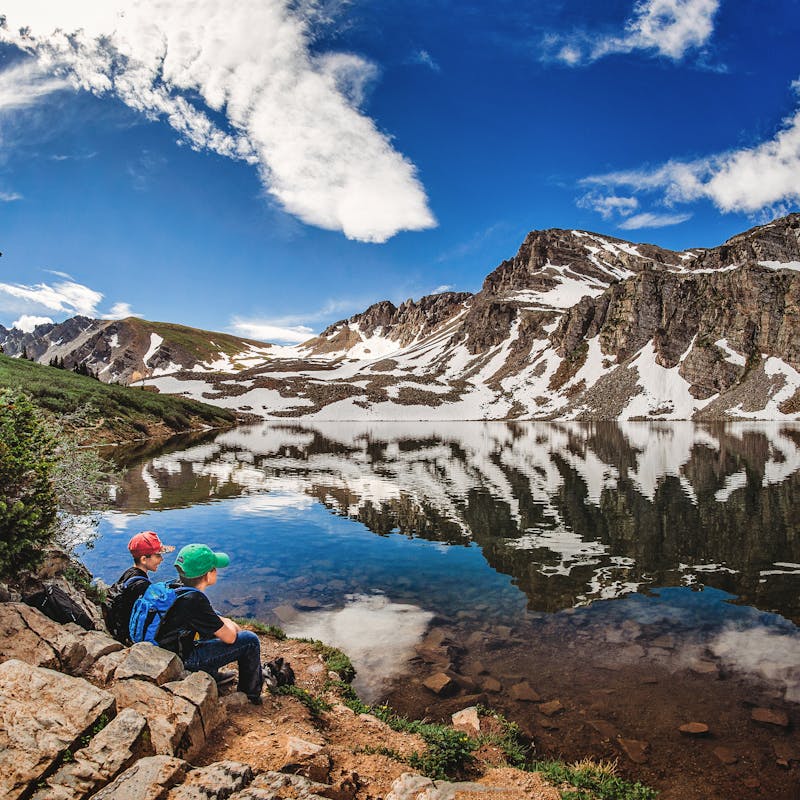Alison Takacs's children sit by a lake with mountains in background.