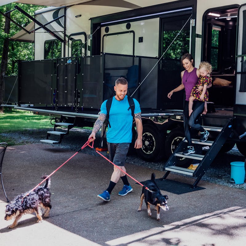 A man, woman and young child coming out of an RV to take two dogs for a walk.