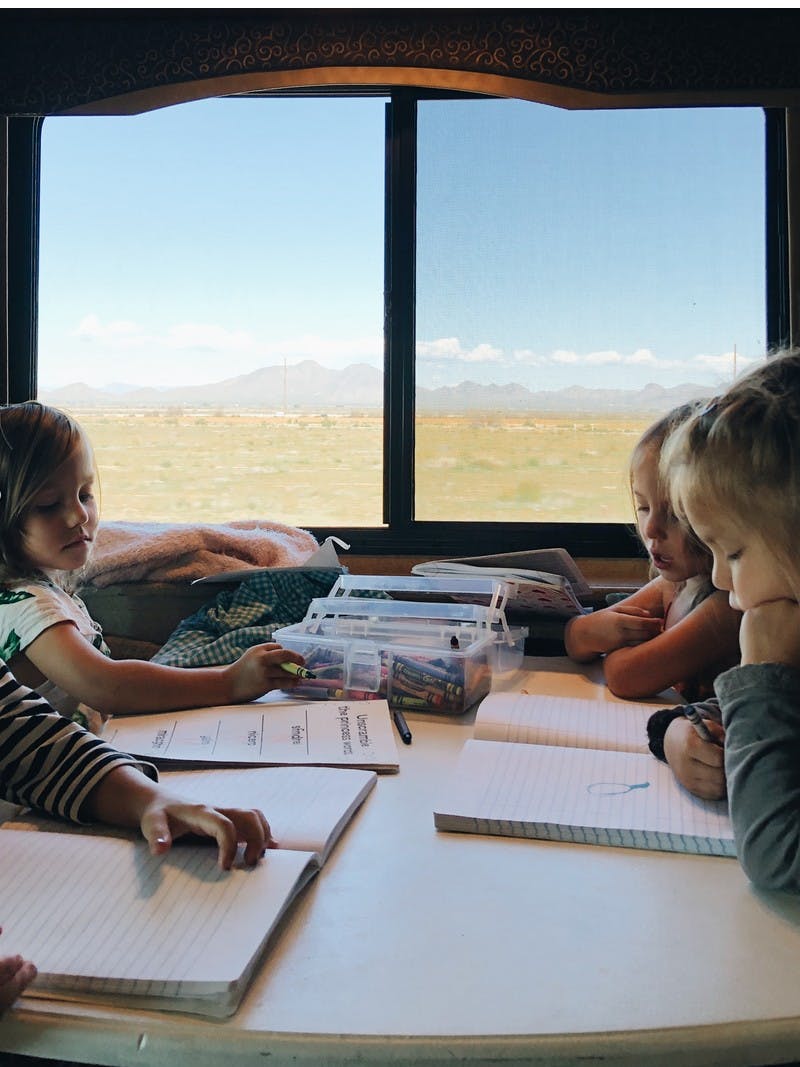 Four young kids sitting at an RV table playing and coloring, with desert mountains out the window.