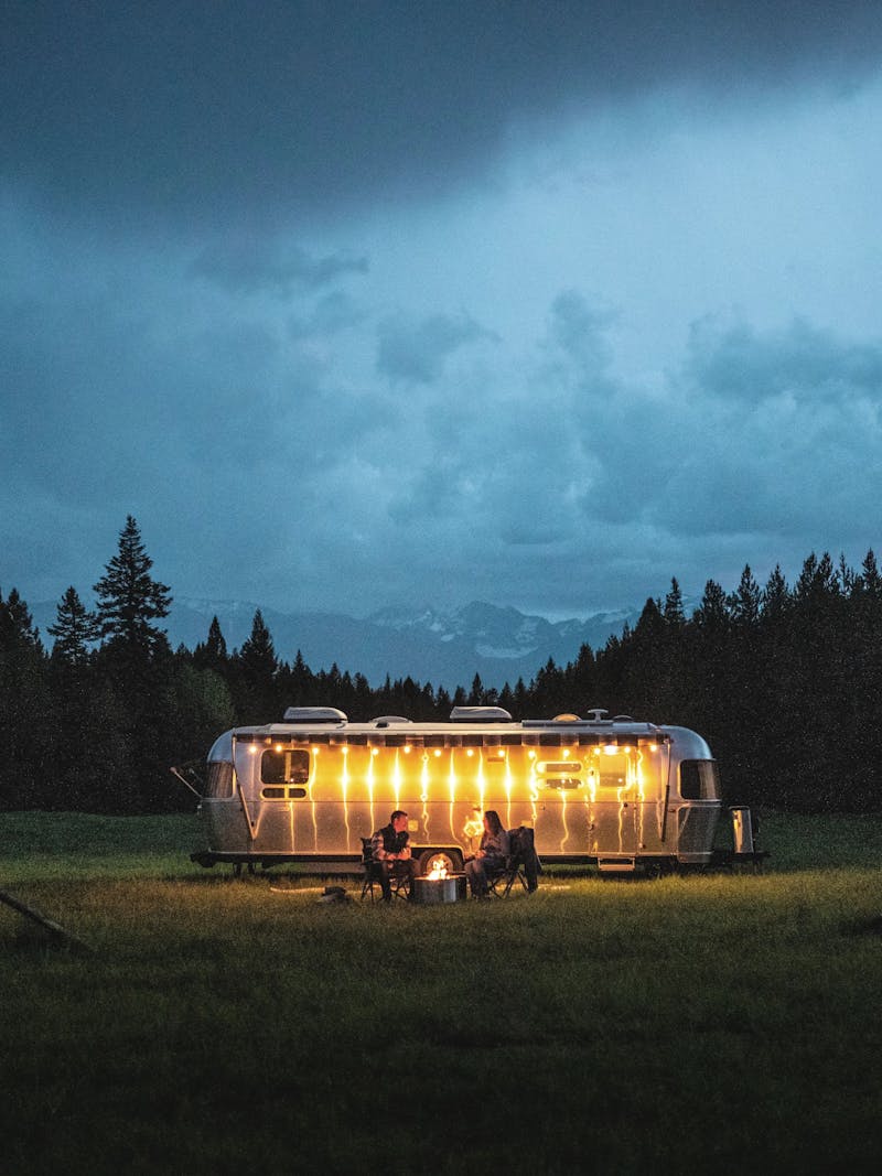 An Airstream travel trailer camping in a field lit up by twinkle lights in the dark sky