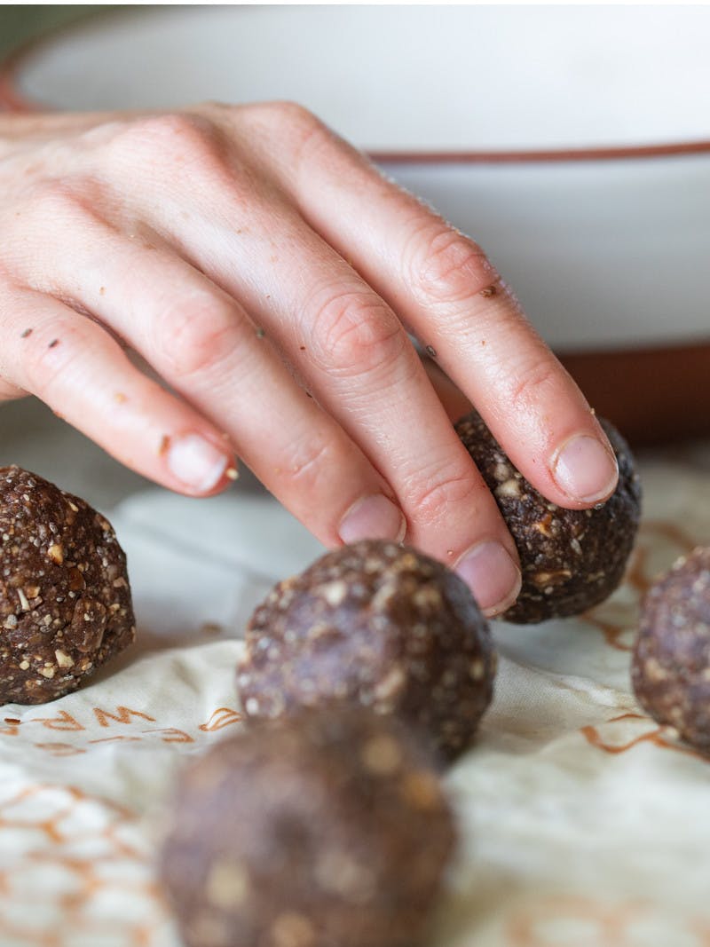Close up of hand placing chia seed balls onto parchment paper with a white bowl in the background.