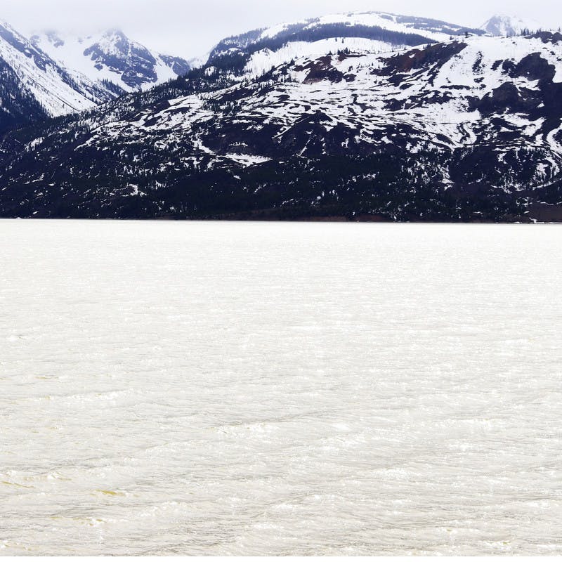 Gray water lake with dark, snowy mountains in the background.