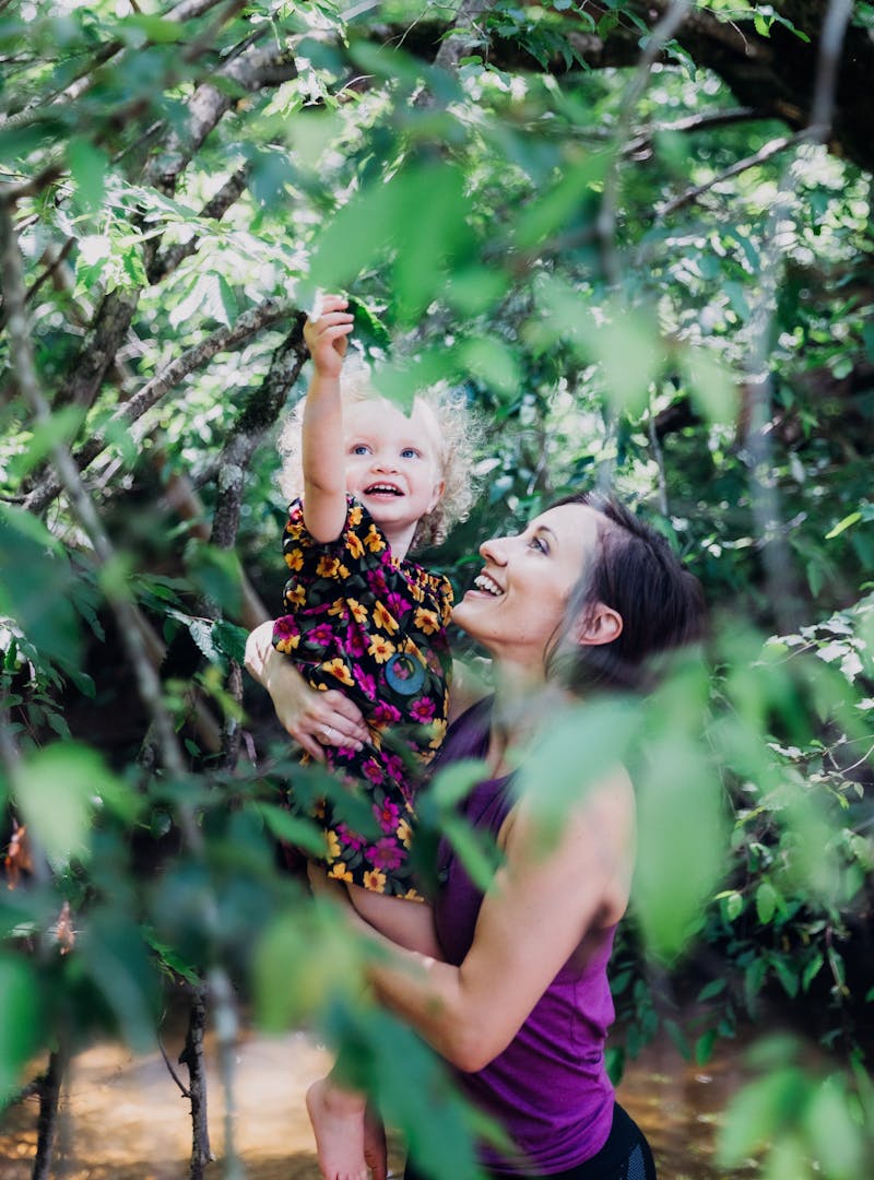 A young mom and her daughter examining a leaf in nature together.