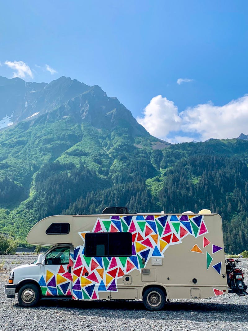 Jason and Dawn's Class C RV parked in a gravel lot near a large mountain.