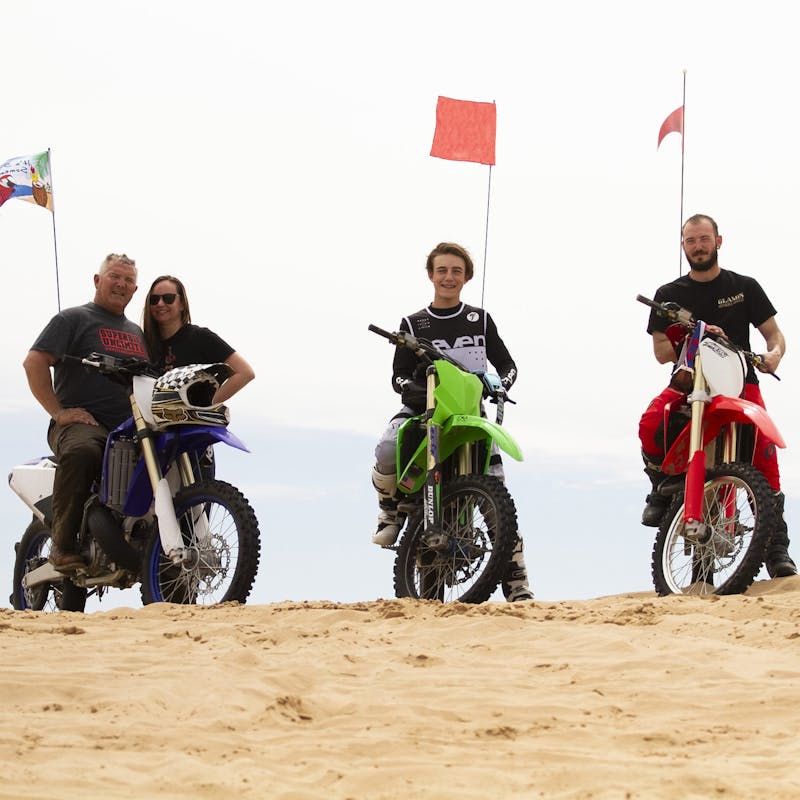 Four people posed on a dune with dirt bikes.