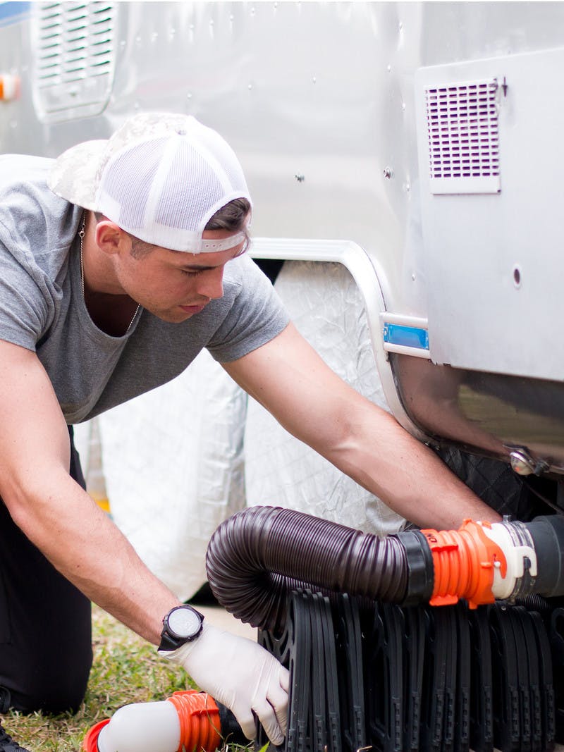 A man hooking up a waste hose to an RV for black water drainage.