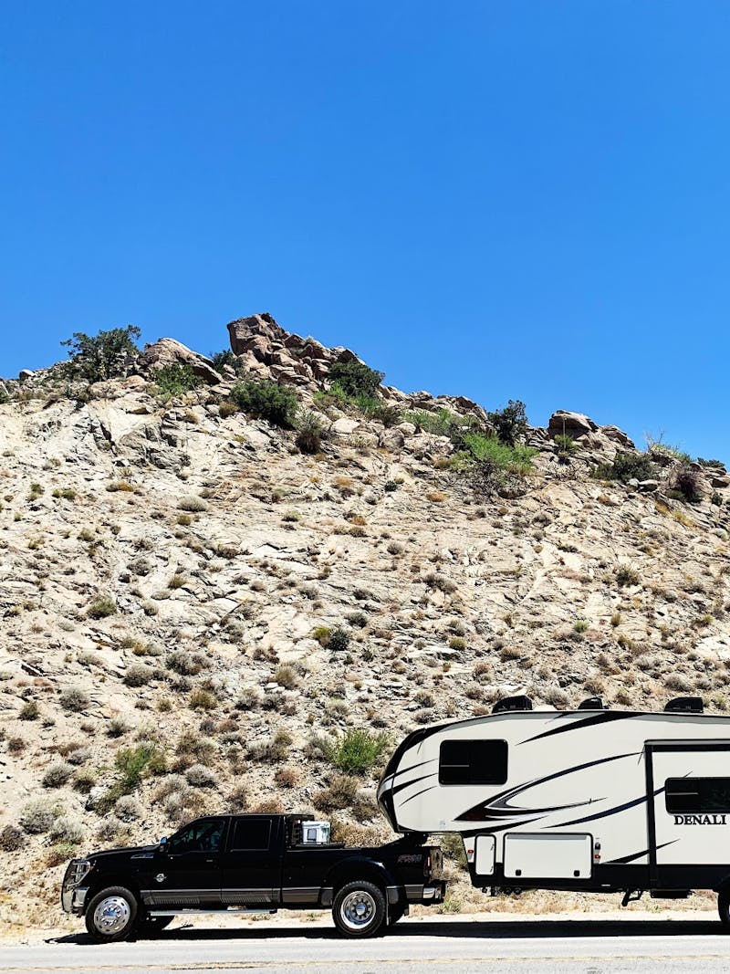 A truck towing an  RV parked in front of a sandy ridge.