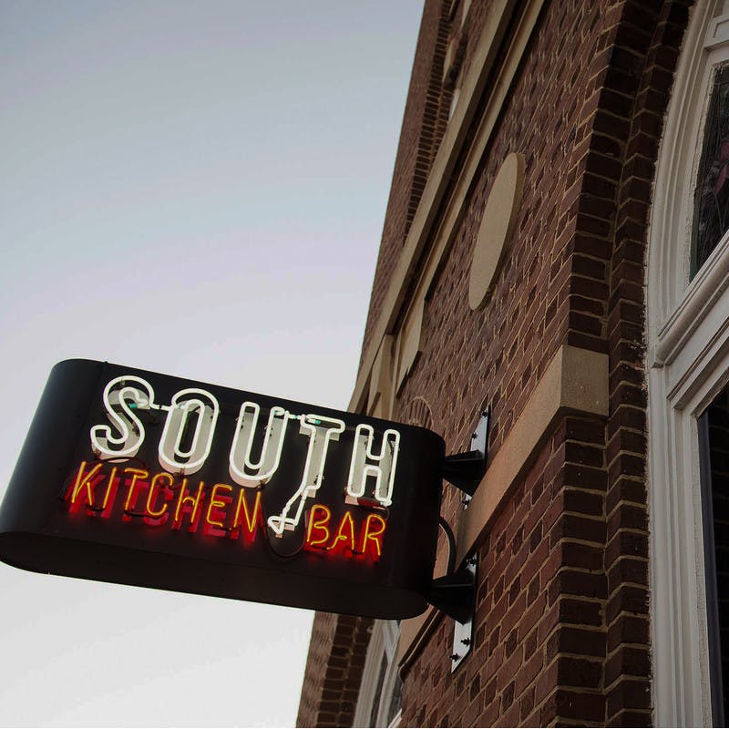 South Kitchen and Bar in Athens, Georgia restaurant brick exterior and front window with neon sign.