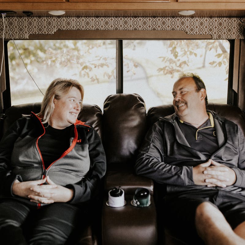 A middle-aged couple sitting in matching recliners inside their RV.