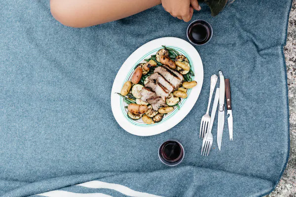 Pork, green beans, and potatoes on a platter with wine and utensils.