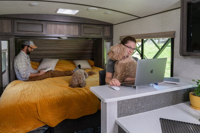 Marcia Schabel works at her computer while Todd reads sitting on the bed inside their Sunset Trail RV.