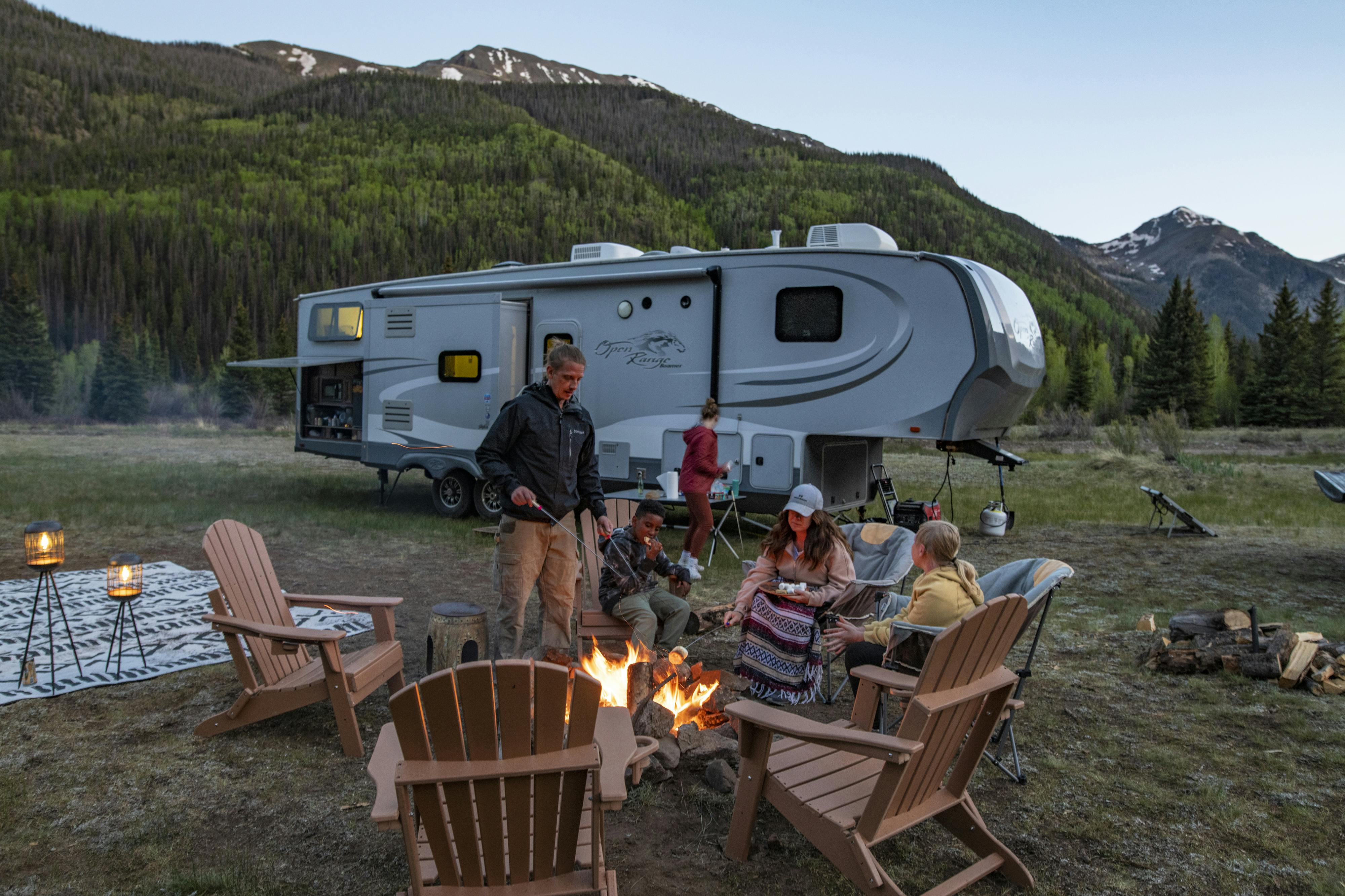 The Carew family sitting around a campfire roasting marshmallows in front of their RV at dusk
