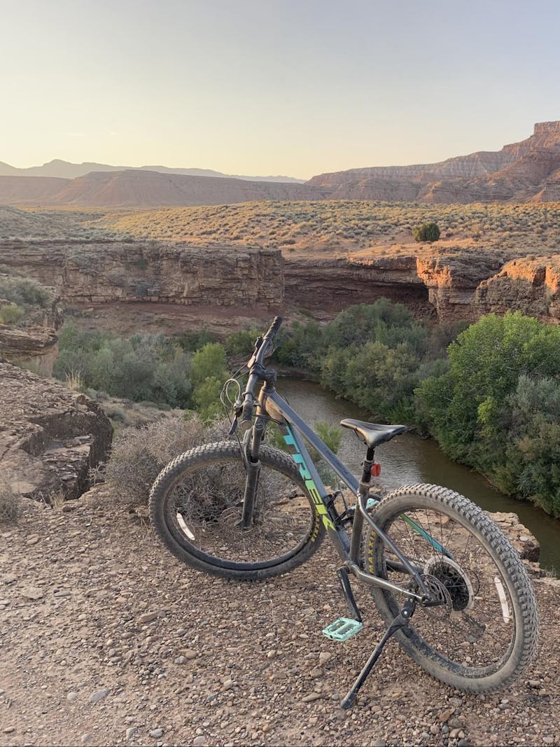 A bike sits on the edge of a cliff overlooking a river and mountains.