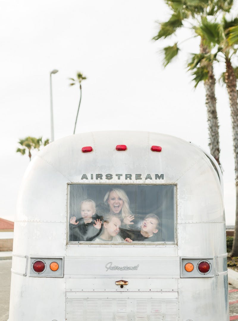 Amber Thrane with three kids, looking out the back window of Airstream RV, with palm trees in the background.