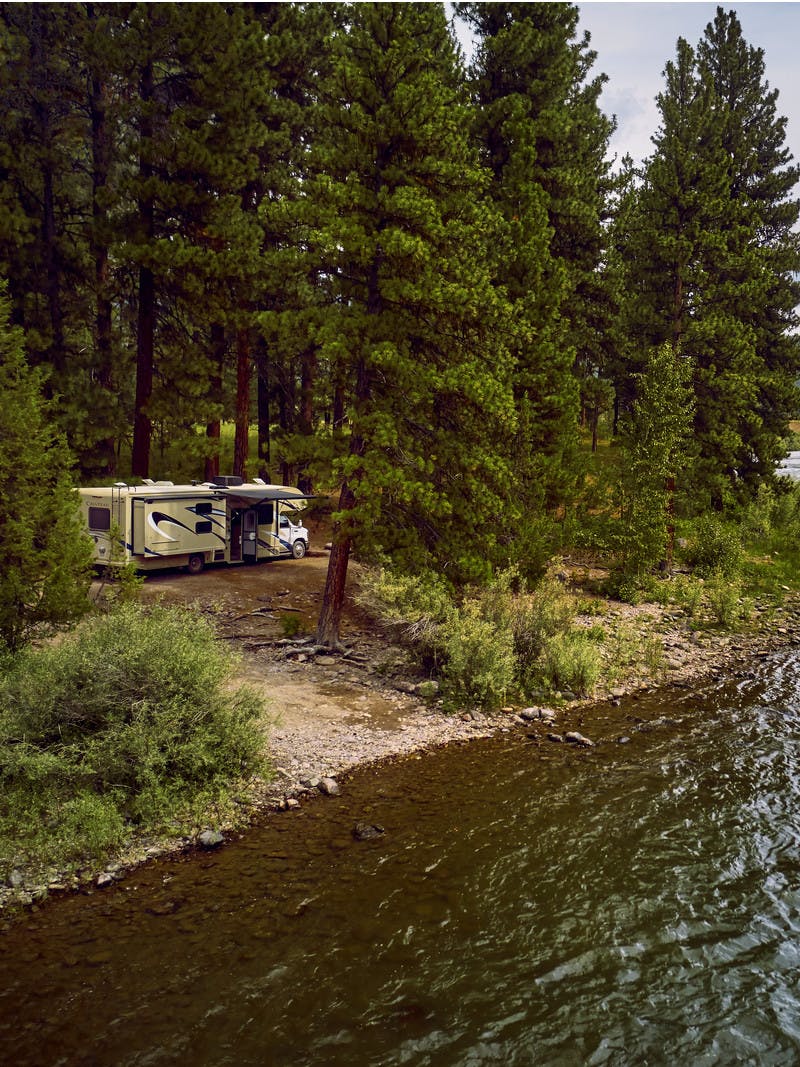 A Class C RV sits next to a bank on the Blackfoot River in Montana.