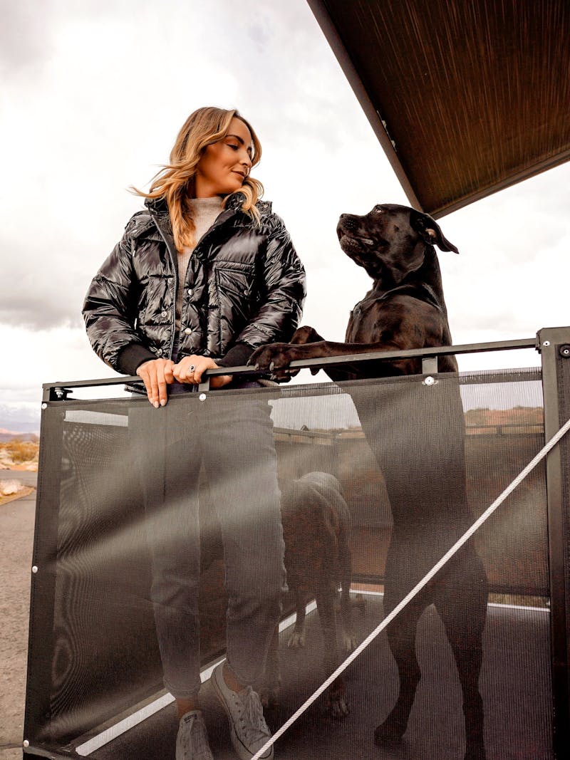 A woman stand on the porch of a toy hauler RV with her dog.
