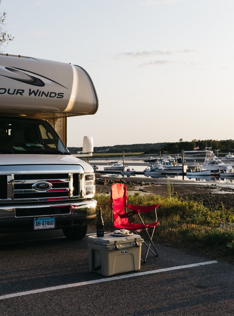 Exterior RV shot alongside a marina with folding chair, Yeti cooler, and beer.