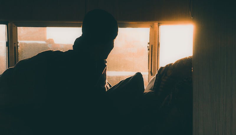Early morning sun shines in an RV window onto a person still in bed.