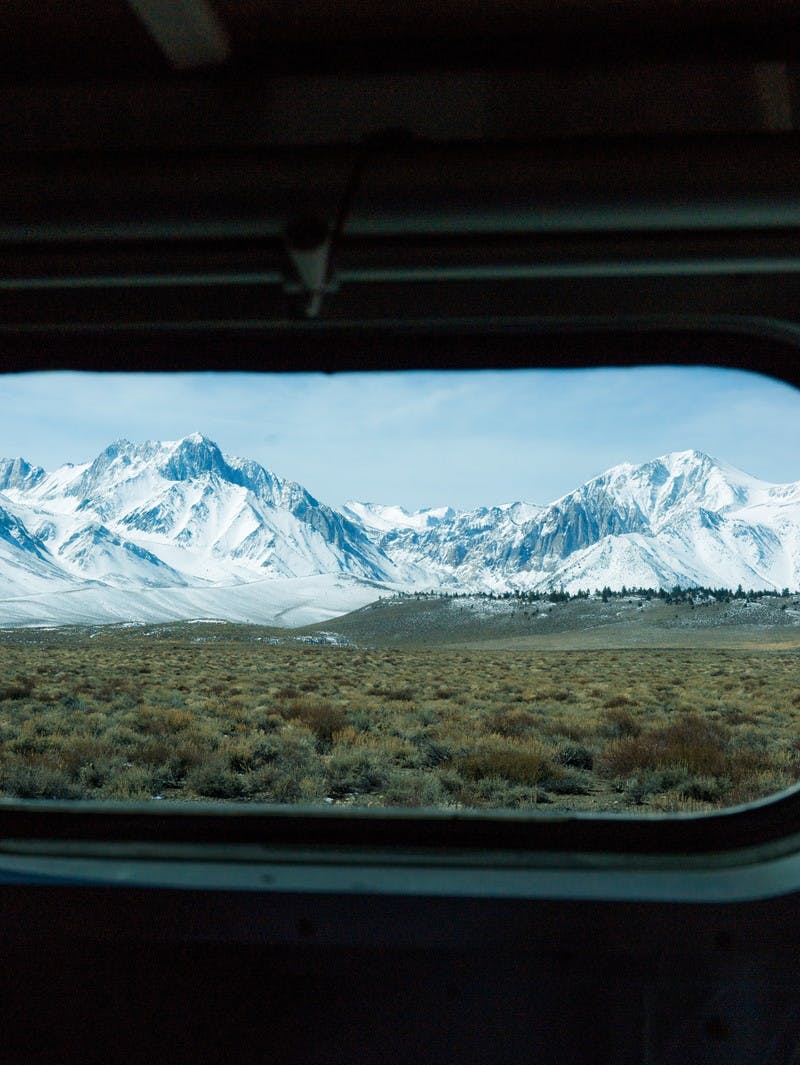 Snowy mountain peaks in the distance, seen through an oblong, rounded RV window.