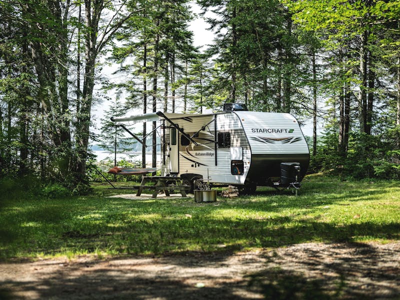 a starcraft lightweight travel travel parked at a campground near a picnic table and a lake in the distance