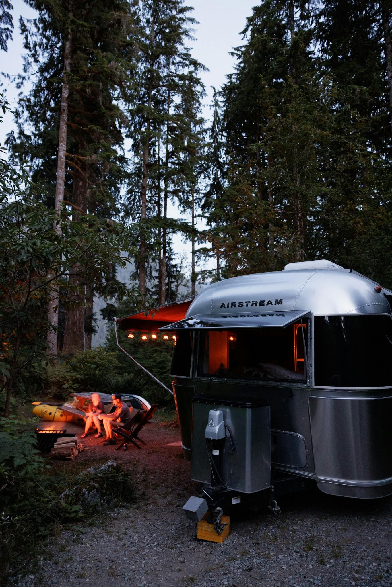 Karen Blue's family sitting by a campfire next to their Airstream travel trailer in a National Forest