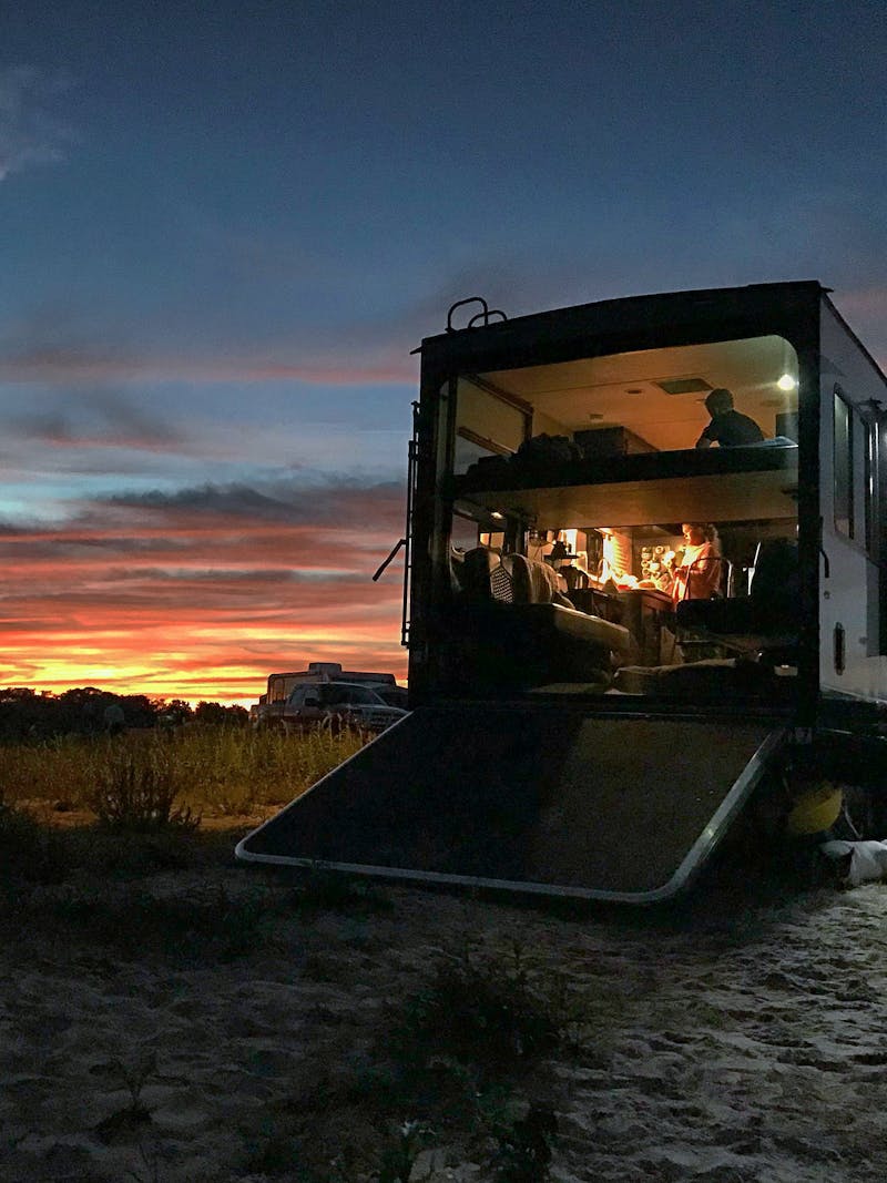 A rainbow sunset over a Toy Hauler RV that's glowing from within with light. 