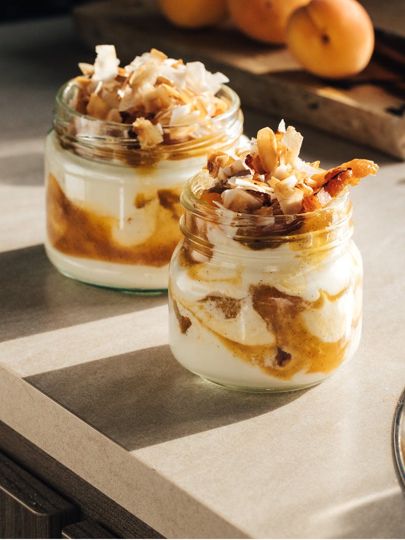 Clear glass jars layered with creamy, white yogurt, golden apricot sauce and toasted coconut flakes.