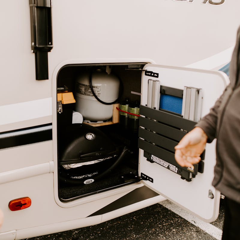 Two people standing outside an open cubby on the exterior of an RV.