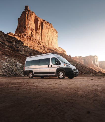 A class B RV parked near large rock formations in the desert. 