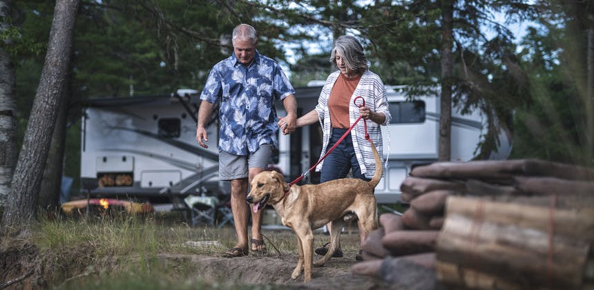 Older couple holding hands with dog walking away from fifth wheel RV in background