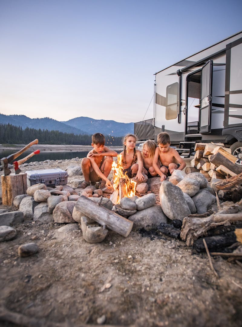 Four children huddled around a campfire in front of an RV.