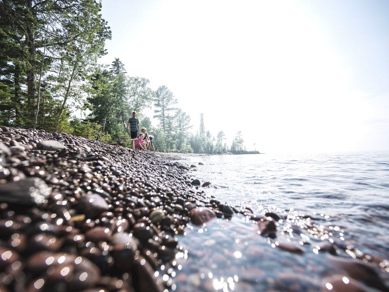 Pebbled lake shore with family skipping rocks