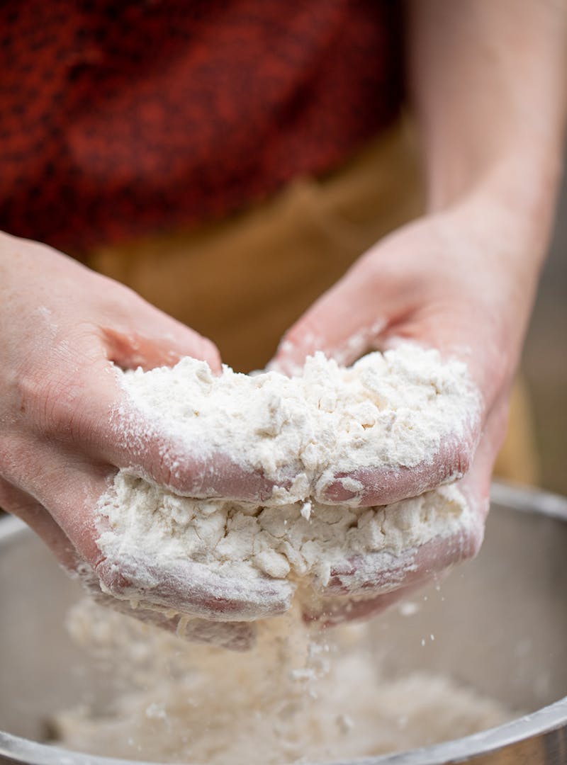 To hands mixing flour and dry ingredients in a bowl.