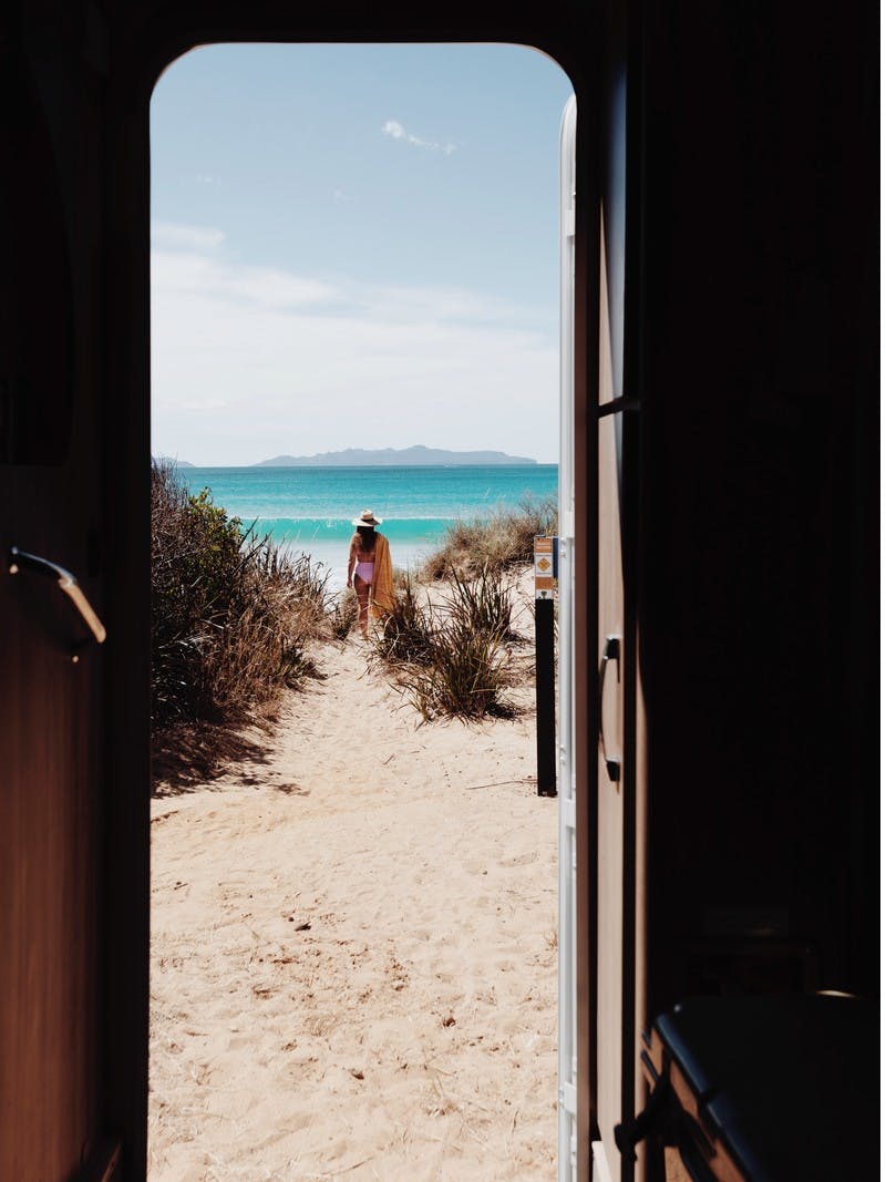A view from the inside of an RV looking out the doorway to Kelvedon Beach, in Tasmania, Australia. With Sarah Glover in the background looking out to the ocean.