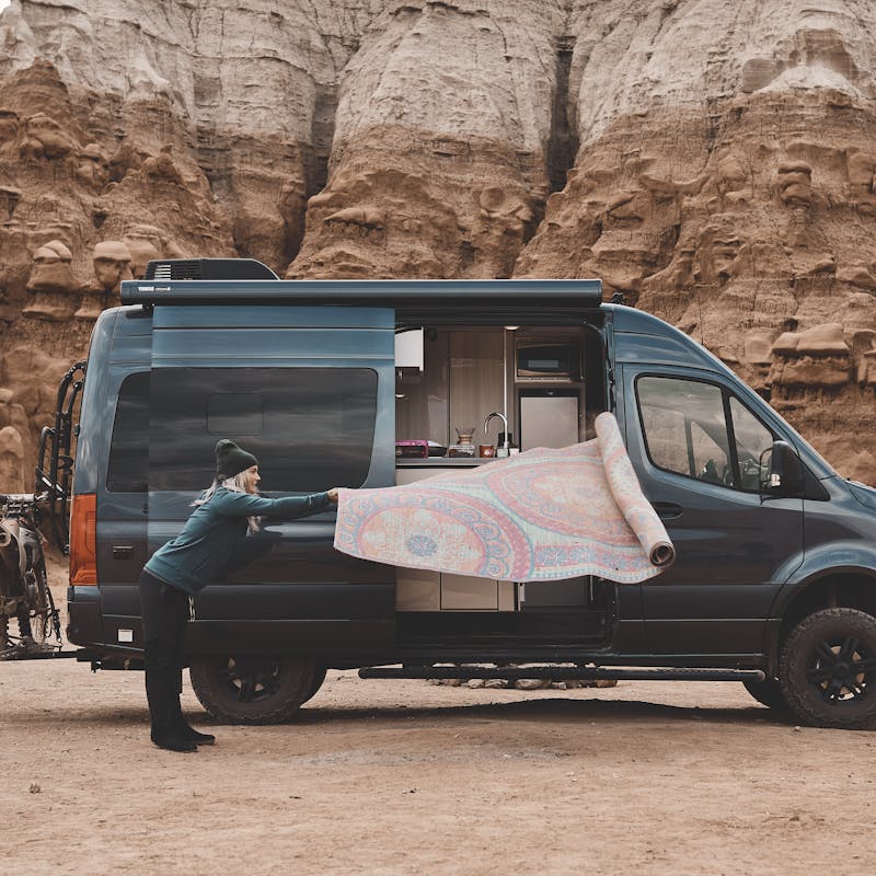 A woman sets out a rug in front of a Class B Van.