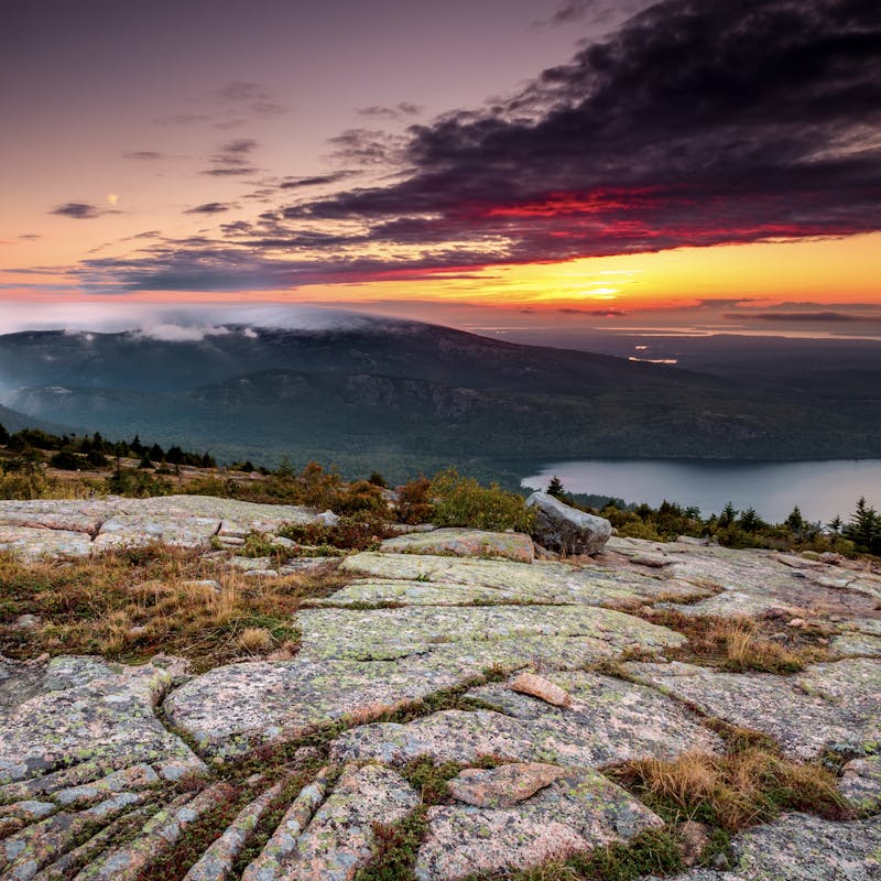 Pink and orange sunset at the top of Cadillac Mountain, overlooking lakes and oceans