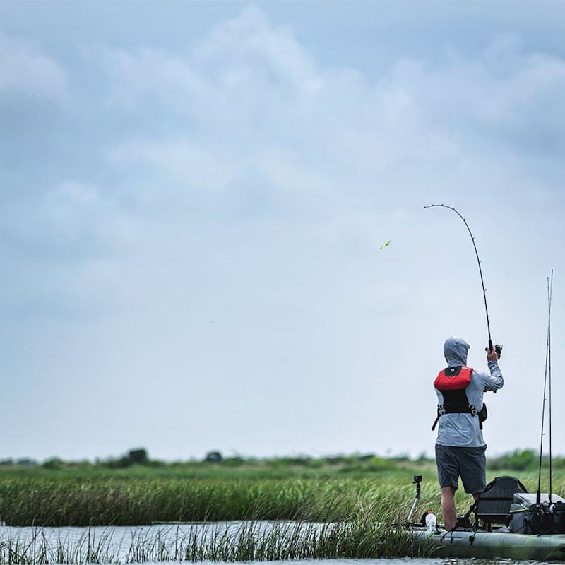 Back of fisherman standing in a kayak casting fishing pole